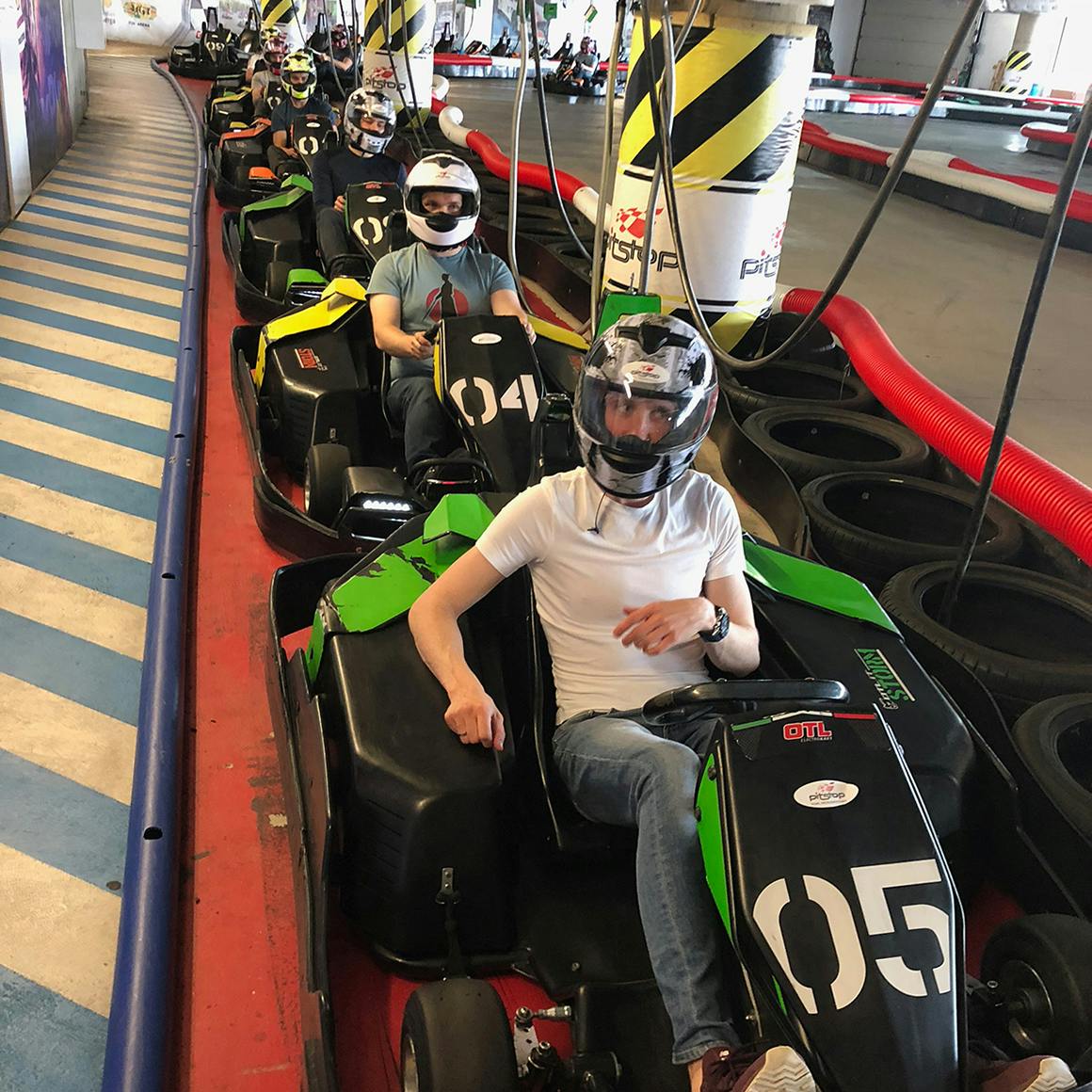 A group of people sitting in go-karts lined up on an indoor karting track.